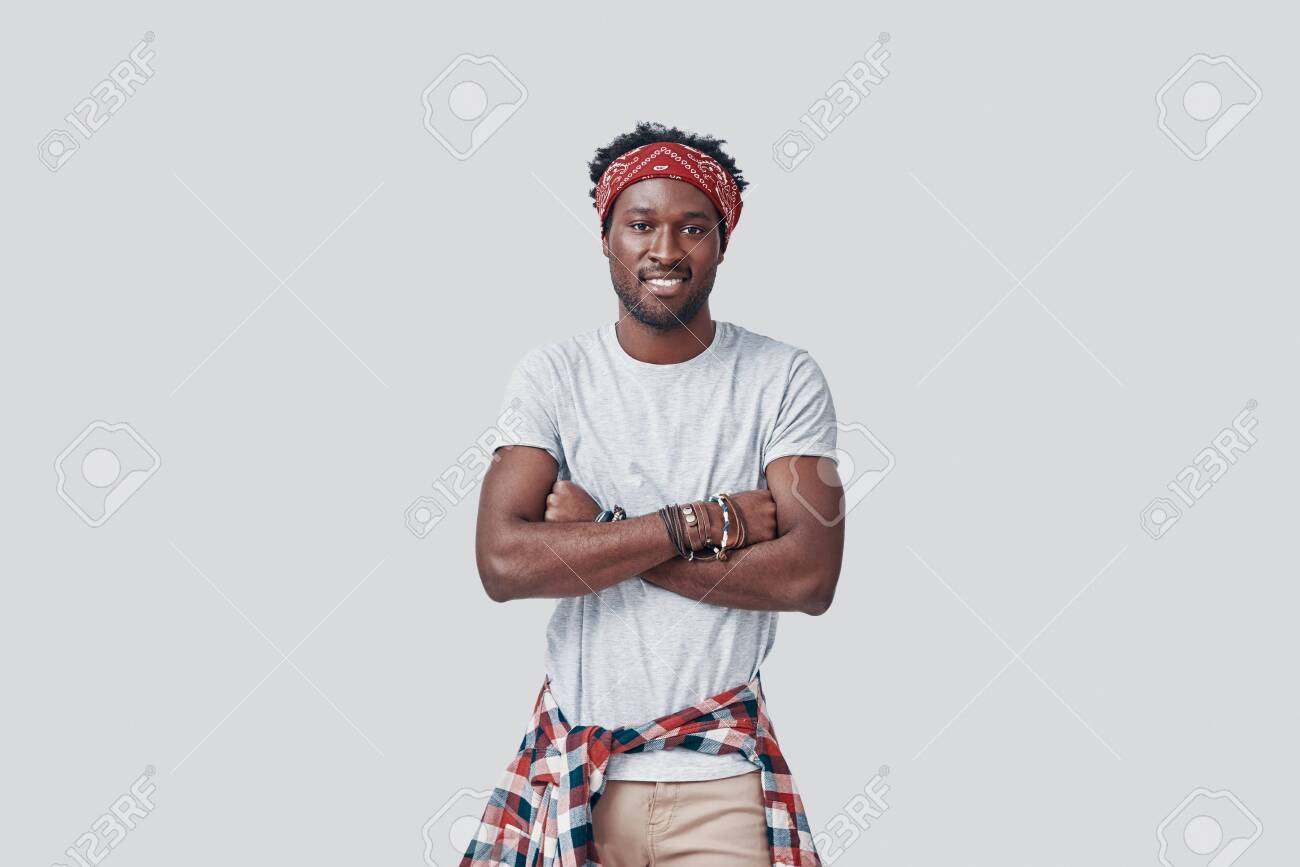 Handsome young African man looking at camera and smiling while standing against grey background - 135471616 Handsome young African man looking at camera and smiling while standing against grey background - 135471616