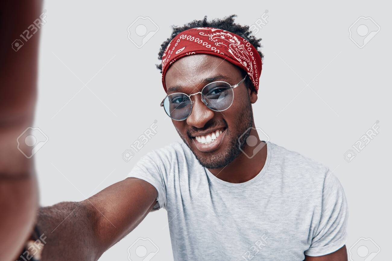 Self portrait of handsome young African man smiling and looking at camera while standing against grey background - 135471628 Self portrait of handsome young African man smiling and looking at camera while standing against grey background - 135471628
