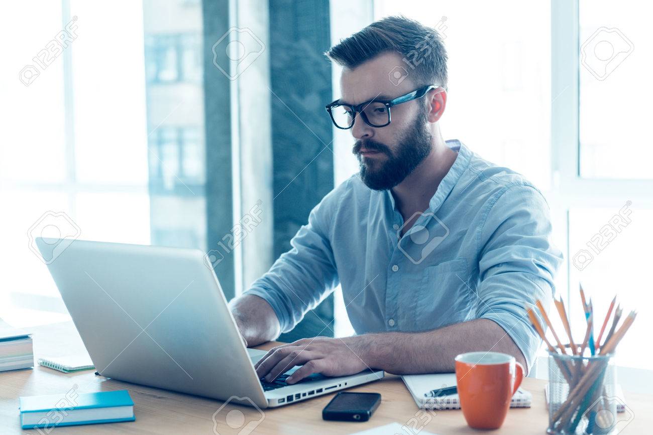 Concentrated On Work. Concentrated Young Beard Man Working On Laptop While  Sitting At His Working Place In Office Stock Photo, Picture And Royalty  Free Image. Image 41257204.