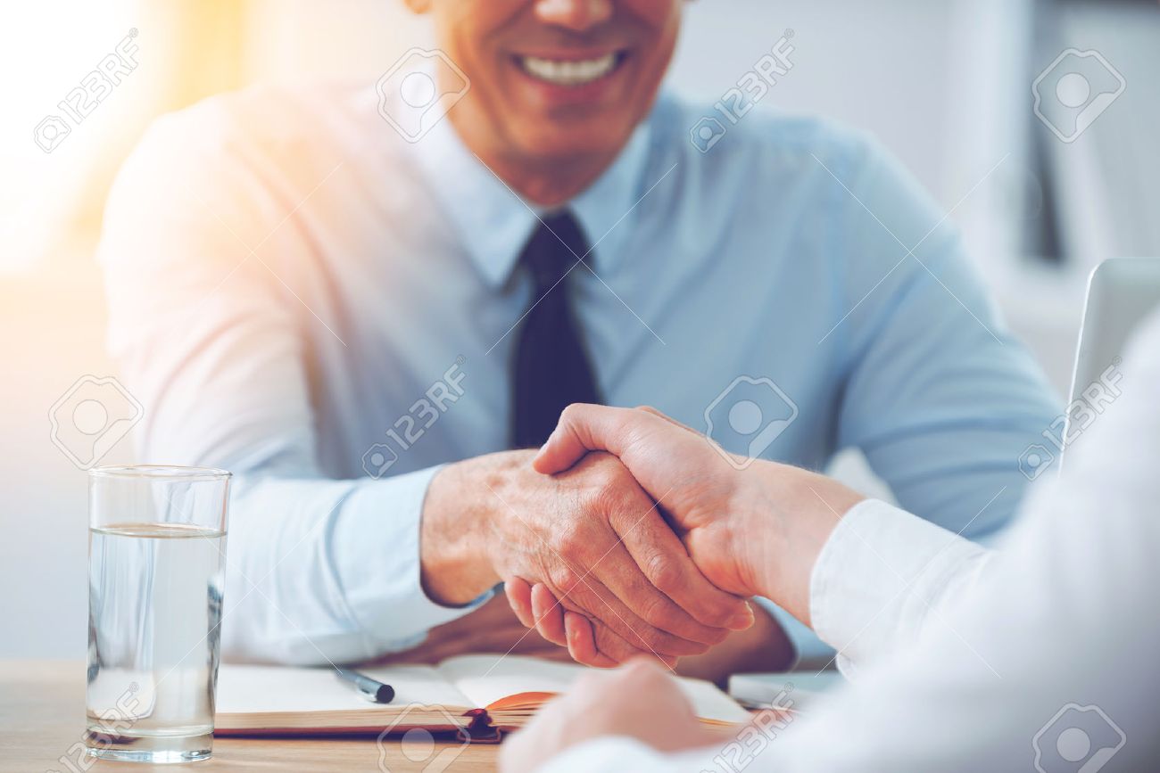 Good deal. Close-up of two business people shaking hands while sitting at the working place - 54625309 Good deal. Close-up of two business people shaking hands while sitting at the working place - 54625309