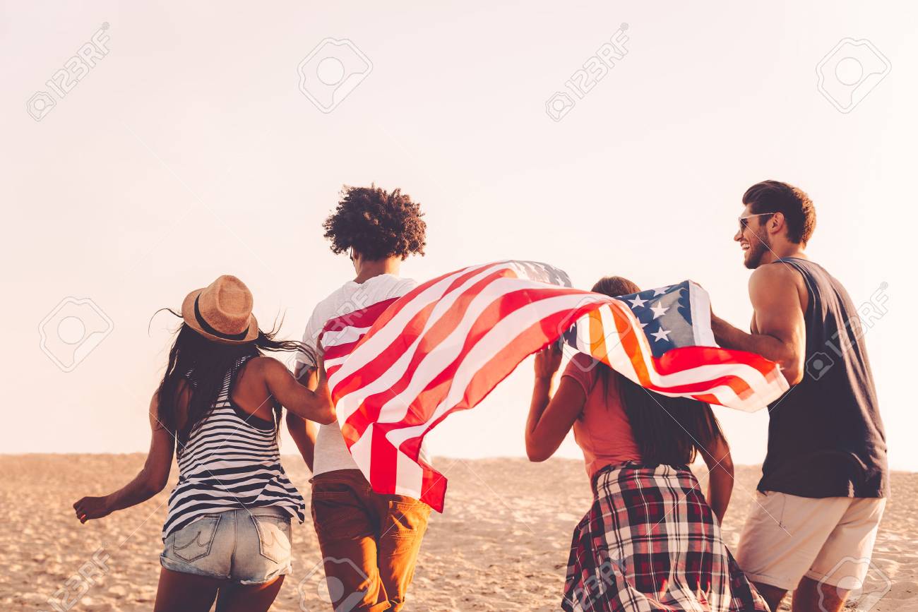 Jung Und Frei Hintere Ansicht Von Vier Jungen Leuten Die Amerikanische Flagge Beim Drausen Jung Und Frei Hintere Ansicht Von Vier Jungen Leuten Die Amerikanische Flagge Beim Drausen