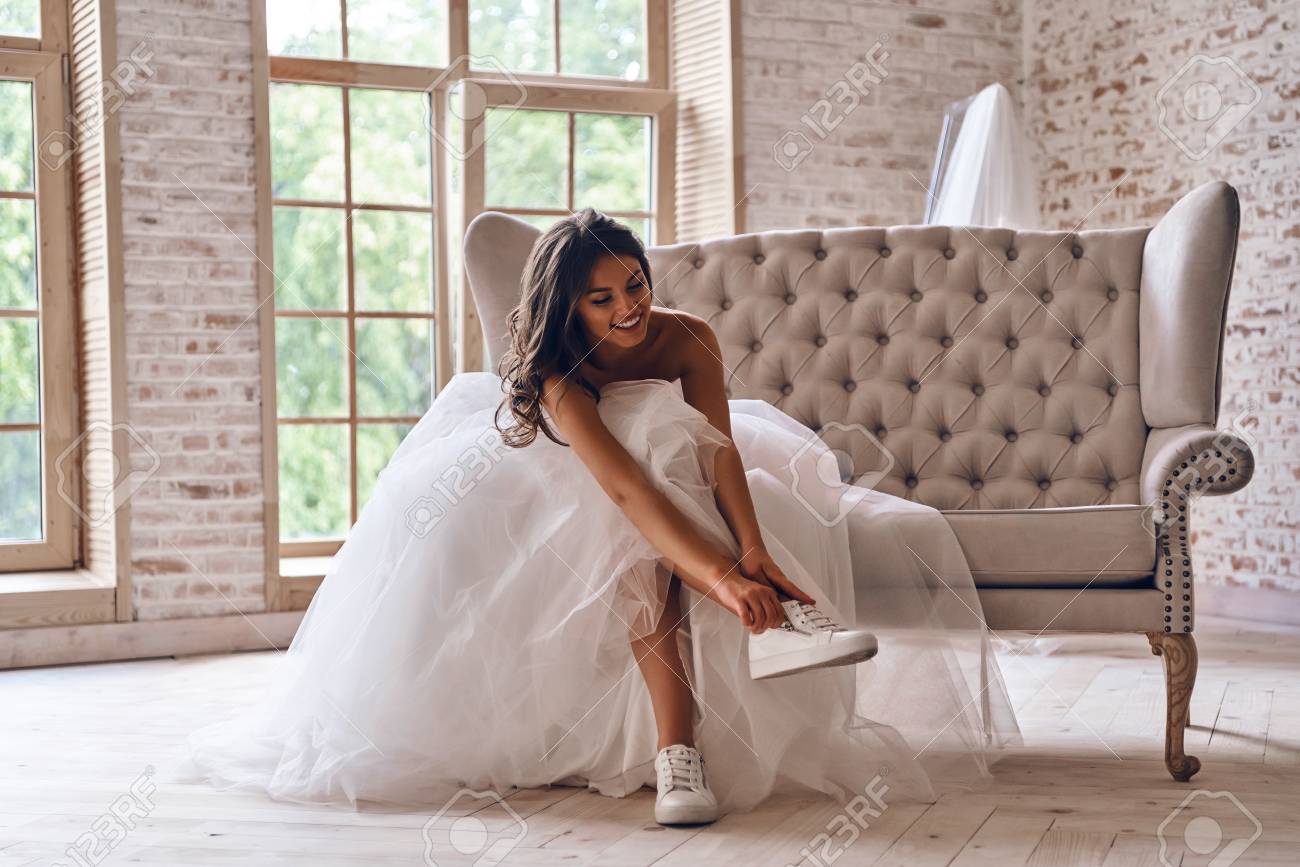 Attractive Young Woman In Wedding Dress Putting On Sports Shoes