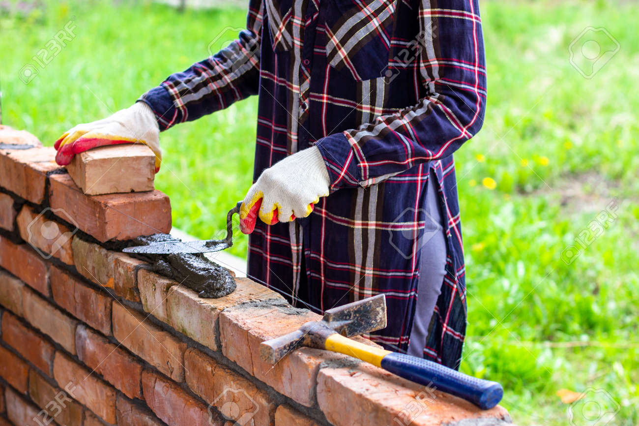 a young female bricklayer lays out cement mortar for laying bricks with a trowel on a brick wall - 169308579 a young female bricklayer lays out cement mortar for laying bricks with a trowel on a brick wall - 169308579