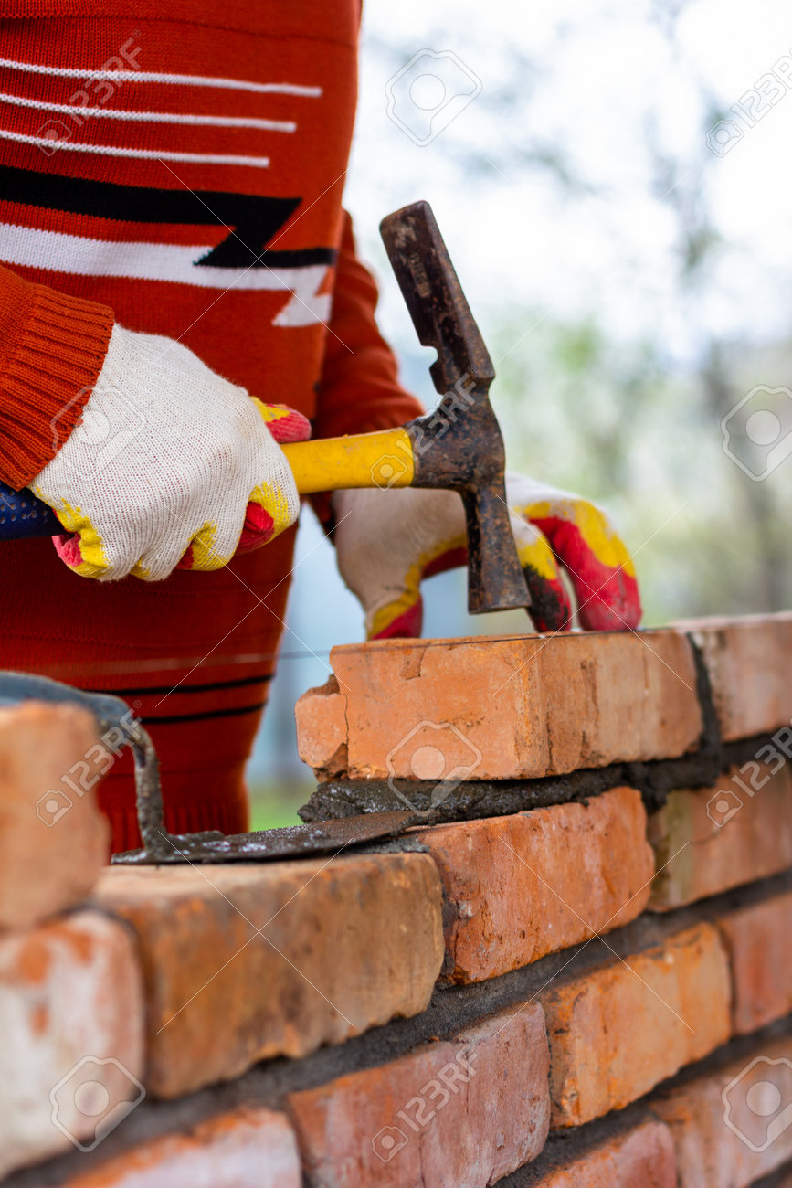 a man builds a brick wall, puts a brick on a cement-sand mortar, tapping a brick with a hammer - 170686167 a man builds a brick wall, puts a brick on a cement-sand mortar, tapping a brick with a hammer - 170686167