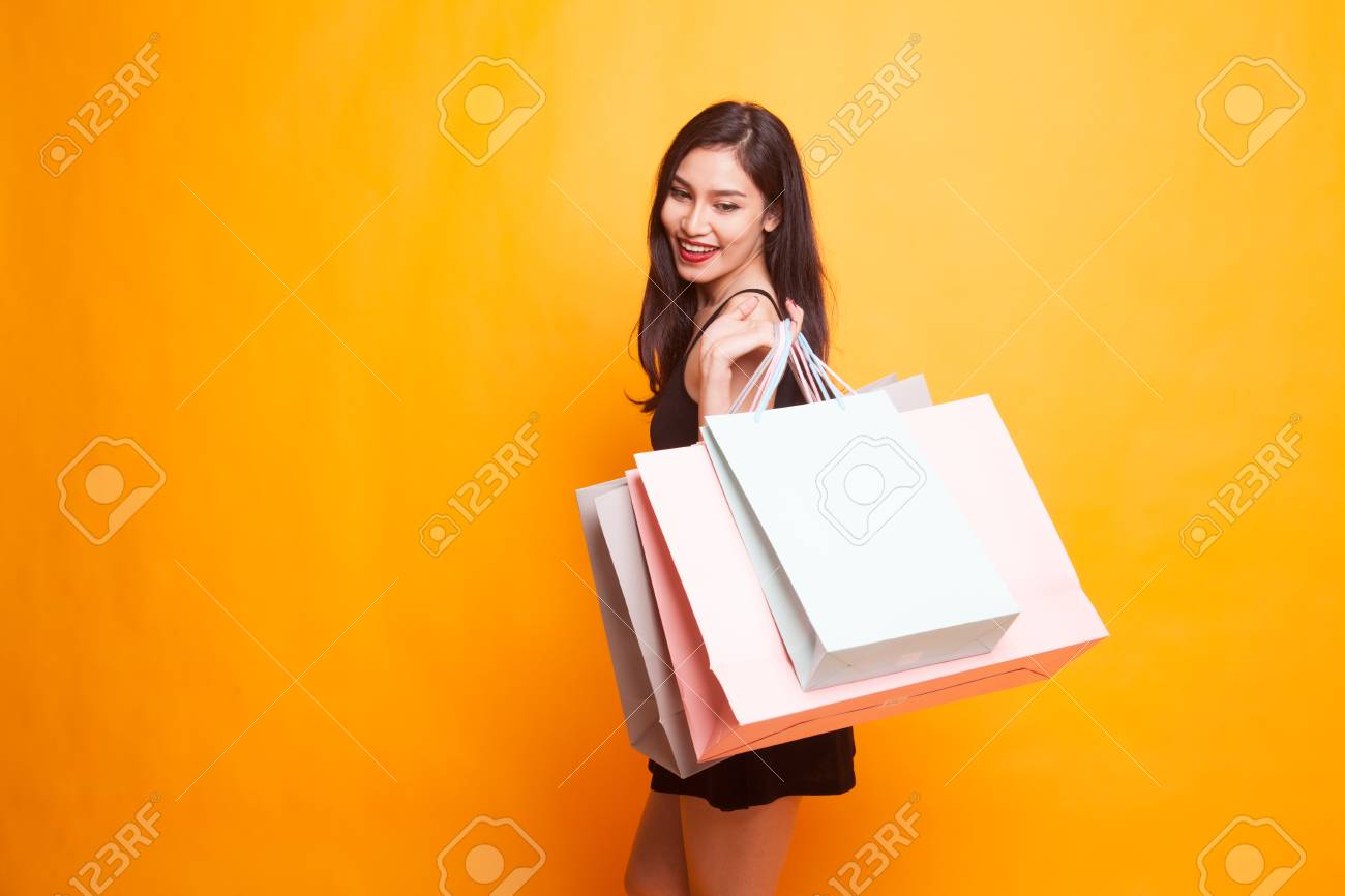 Young Asian woman happy with shopping bag on yellow background - 99895832 Young Asian woman happy with shopping bag on yellow background - 99895832