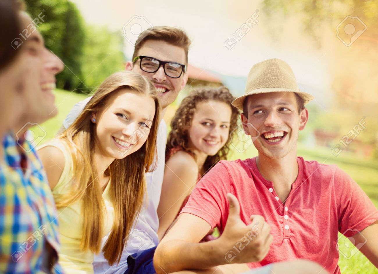 group of young people having fun in park sitting on the grass stock