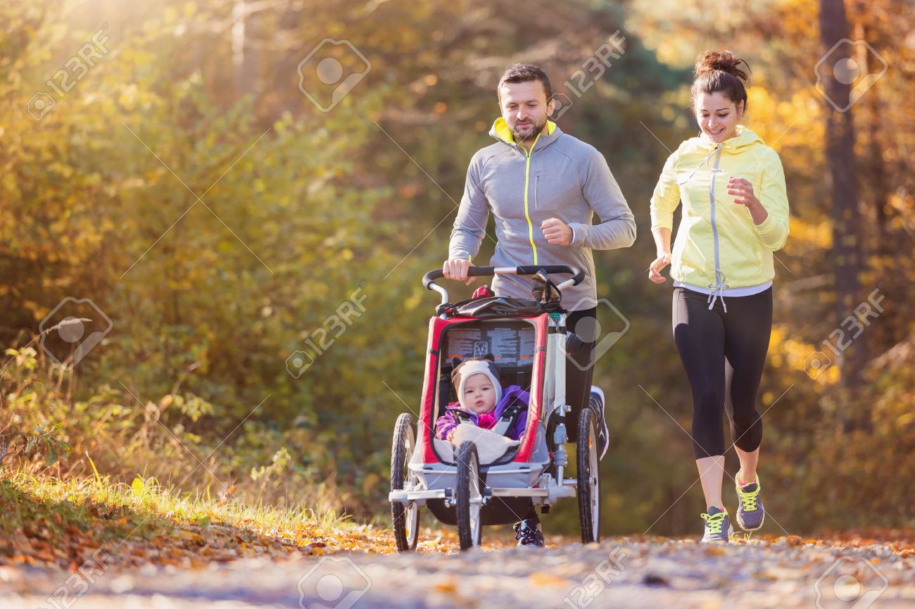 Beautiful young family with baby in jogging stroller running outside in autumn nature - 50204808 Beautiful young family with baby in jogging stroller running outside in autumn nature - 50204808