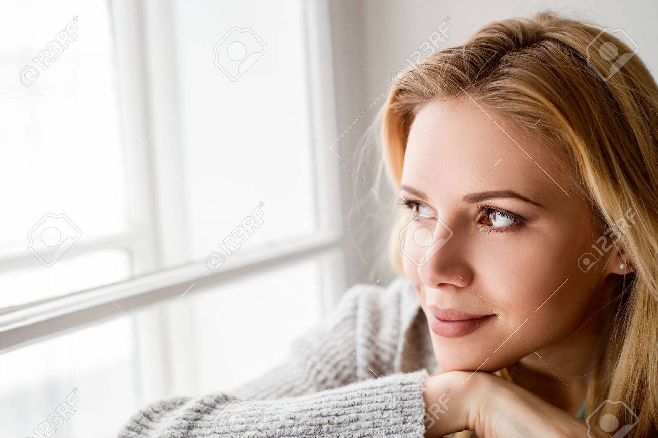 Beautiful blond woman sitting on window sill, looking out of window - 54065285 Beautiful blond woman sitting on window sill, looking out of window - 54065285