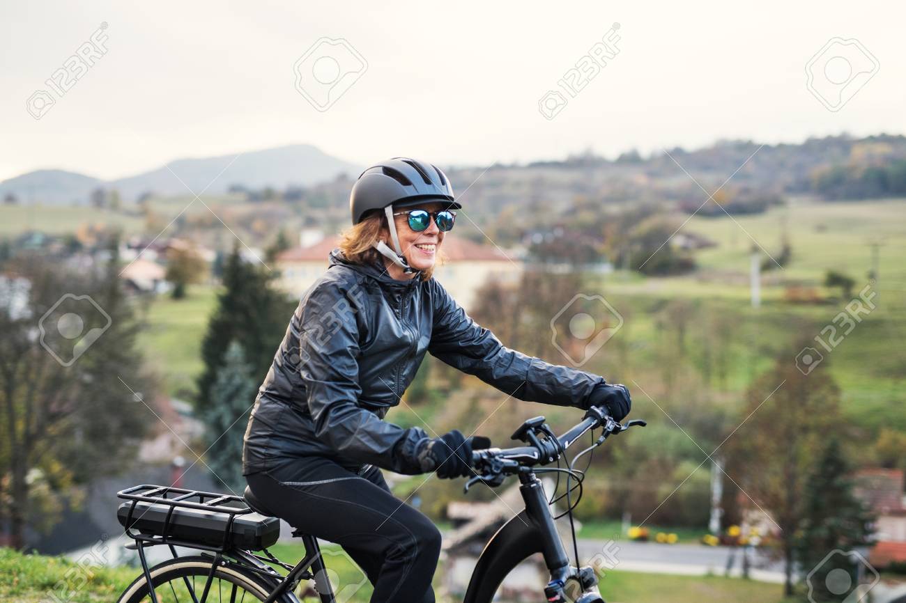 A side view of senior woman with electrobike cycling outdoors in countryside. - 116367110 A side view of senior woman with electrobike cycling outdoors in countryside. - 116367110