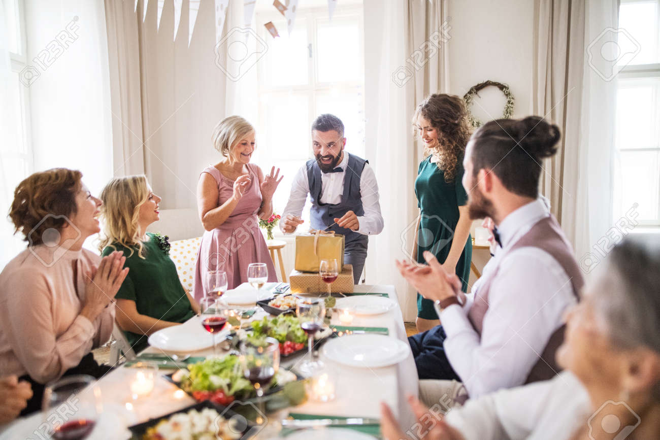 A mature man with friends and family opening presents on a birthday party. - 119973071 A mature man with friends and family opening presents on a birthday party. - 119973071