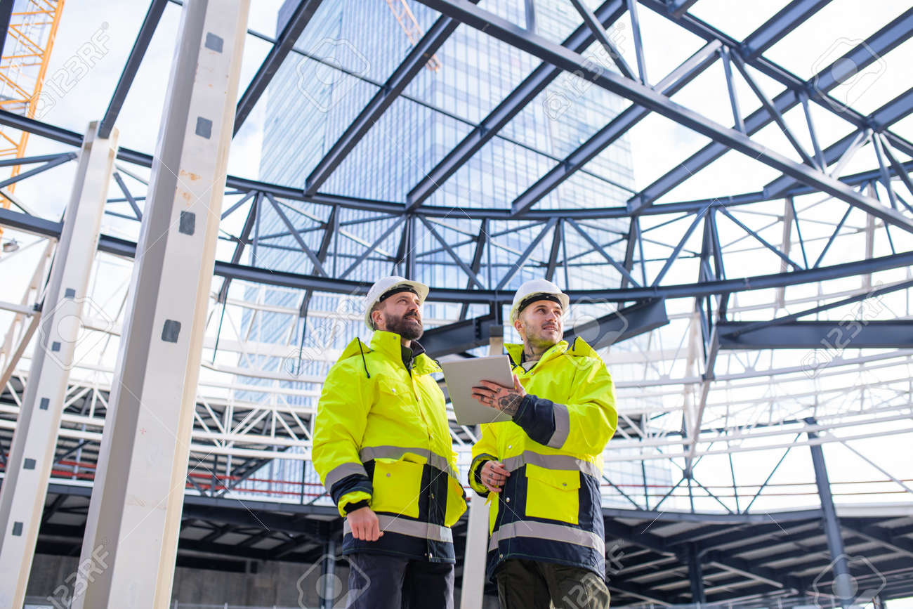 Men engineers standing outdoors on construction site, using tablet. - 139930301 Men engineers standing outdoors on construction site, using tablet. - 139930301