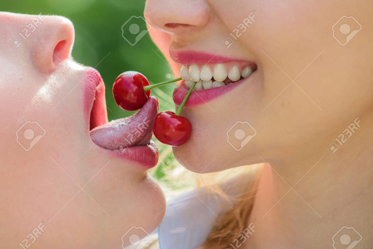 Lesbian Story. Cherries In The Female Mouth Concept. Passion And Love.  Homosexual Couple. Delicious Food Date. Erotica Lgbt. Female Sensual Tongue  And Lips. Lick Cherry. Two Beautiful Women Close Up. Stock Photo,