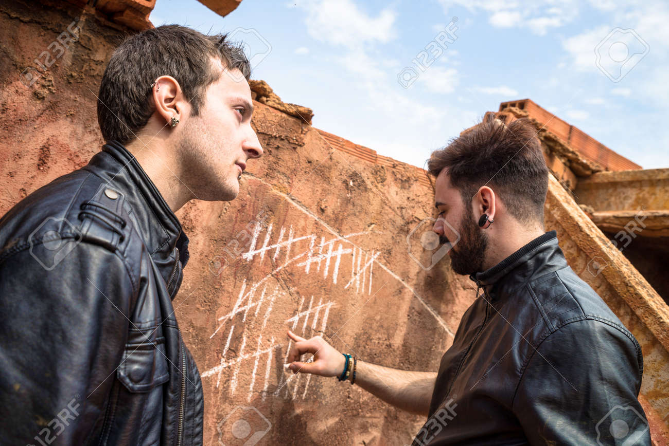 two guys couning days with chalk markings on a wall stock photo