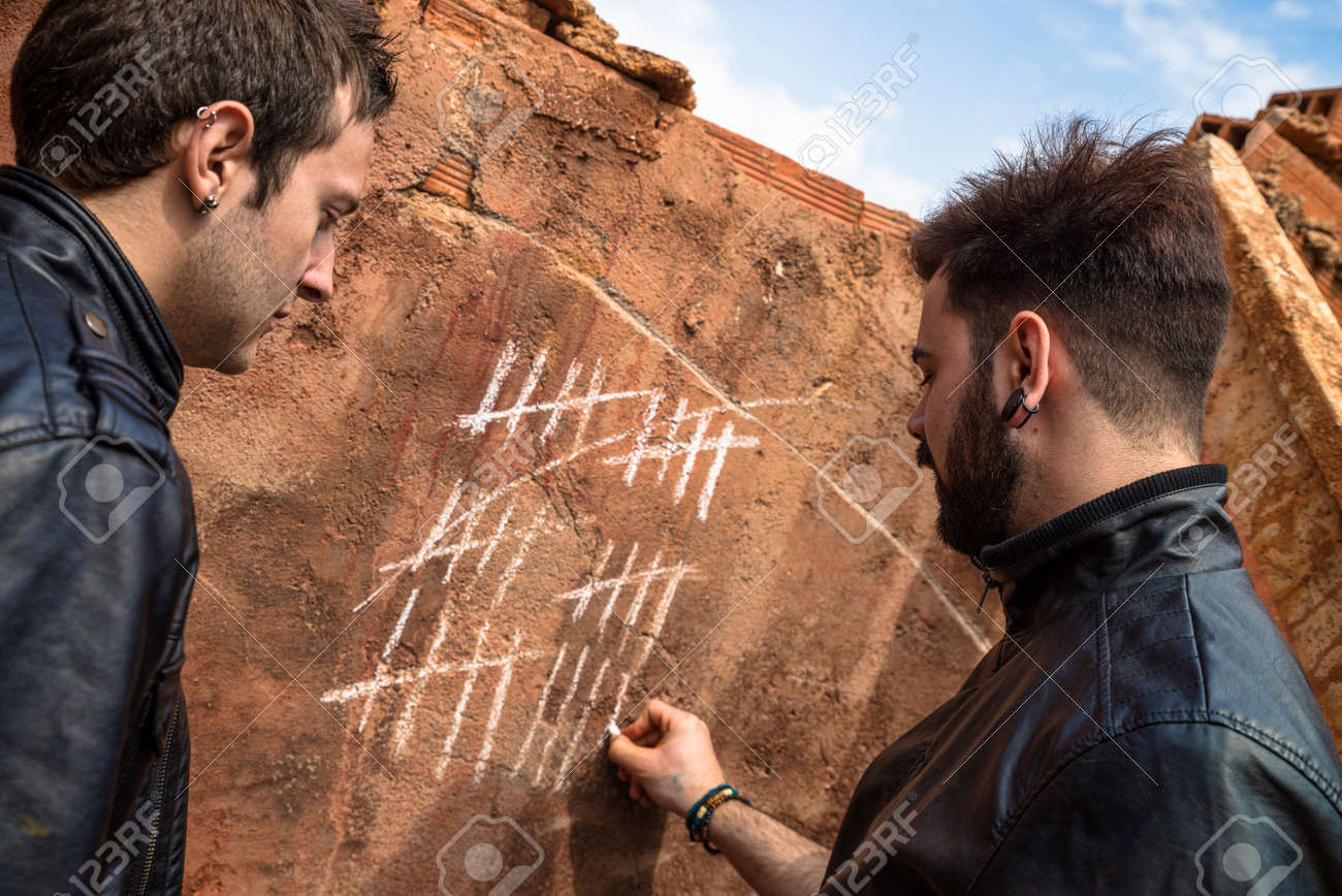two guys couning days with chalk markings on a wall stock photo