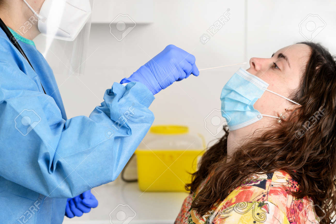 Nurse in a protective suit takes a nasal swab sample from a young female patient. concept. - 167629065 Nurse in a protective suit takes a nasal swab sample from a young female patient. concept. - 167629065