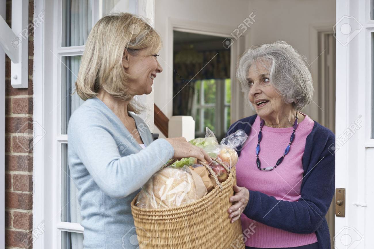 Female Neighbor Helping Senior Woman With Shopping - 57482854 Female Neighbor Helping Senior Woman With Shopping - 57482854