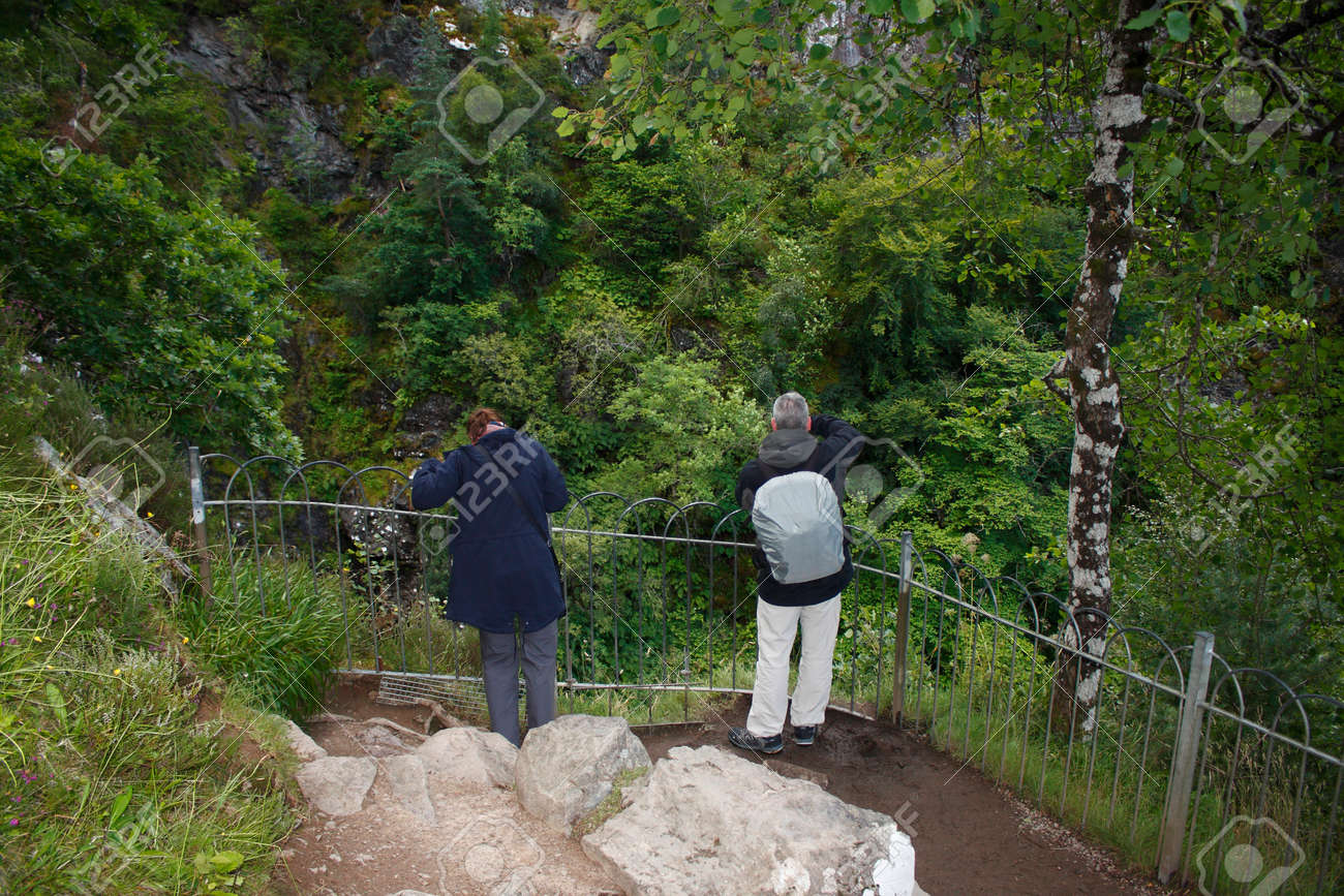 A Man And A Woman Standing In The Vantage Point Of The Waterfall