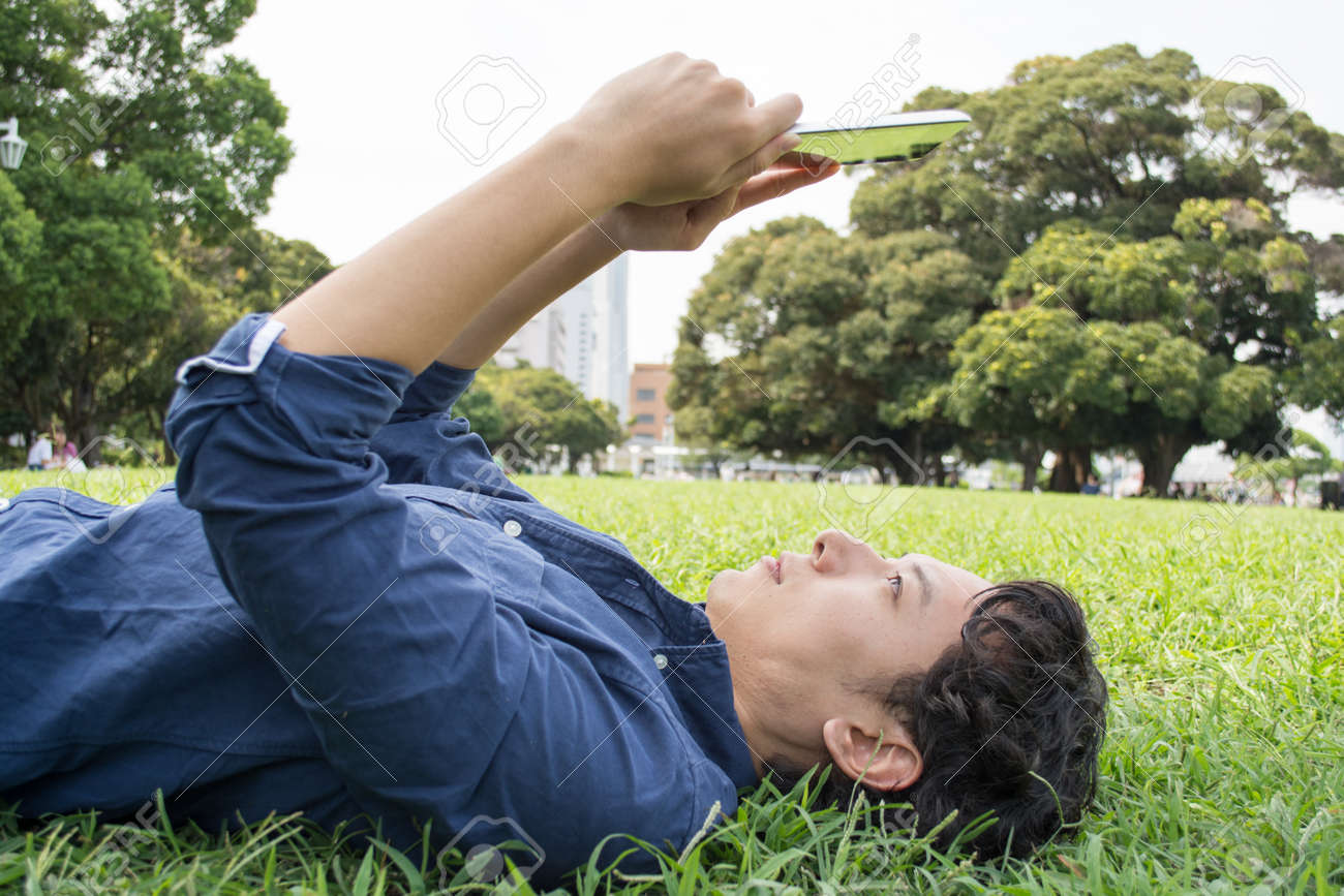 アジア系の若いフリーランスの人 芝生の上を敷設とタブレットを使用して の写真素材 画像素材 Image