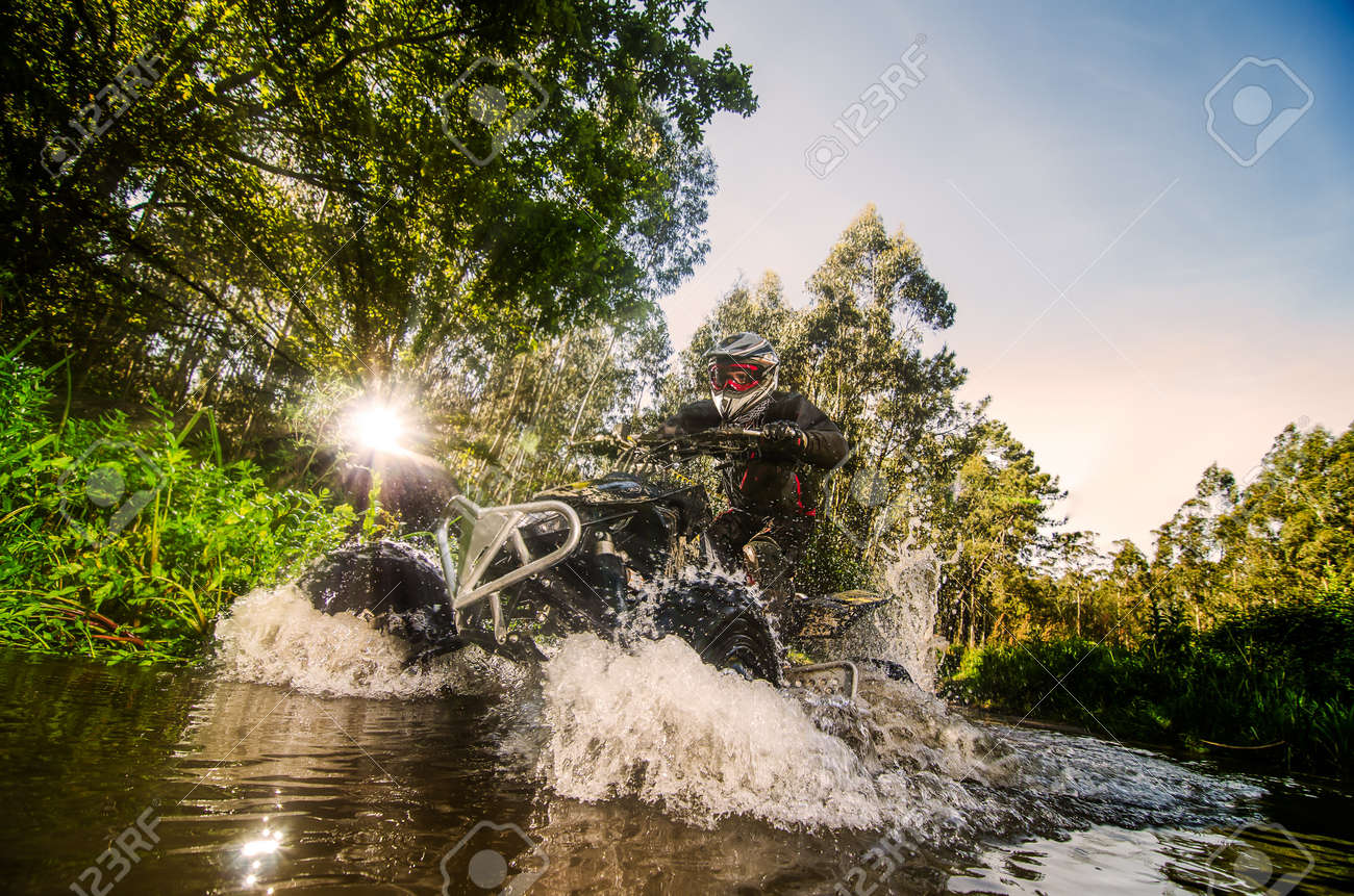 Quad rider through water stream in the forest against sunlight. - 19224029 Quad rider through water stream in the forest against sunlight. - 19224029