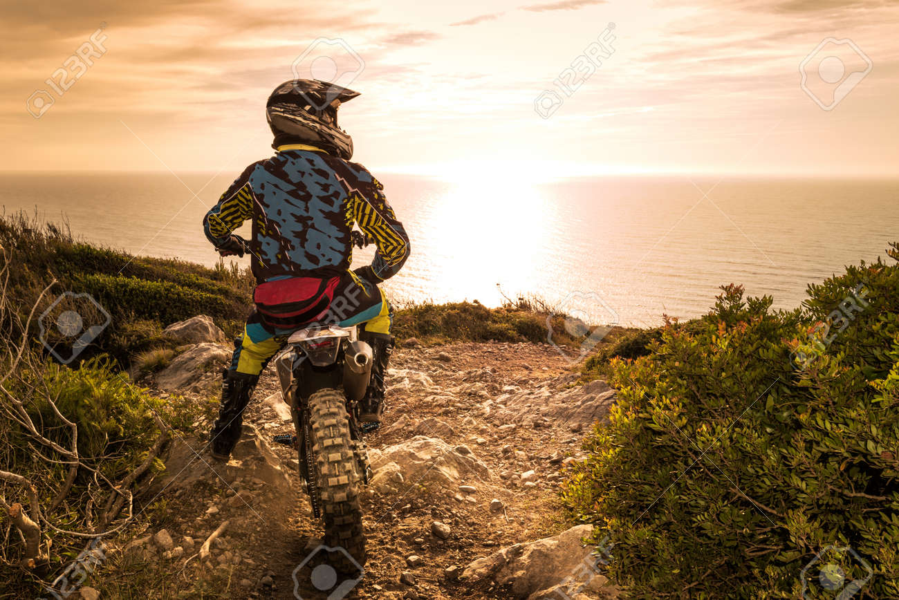 Enduro racer sitting on his motorcycle watching the sunset. - 40309101 Enduro racer sitting on his motorcycle watching the sunset. - 40309101