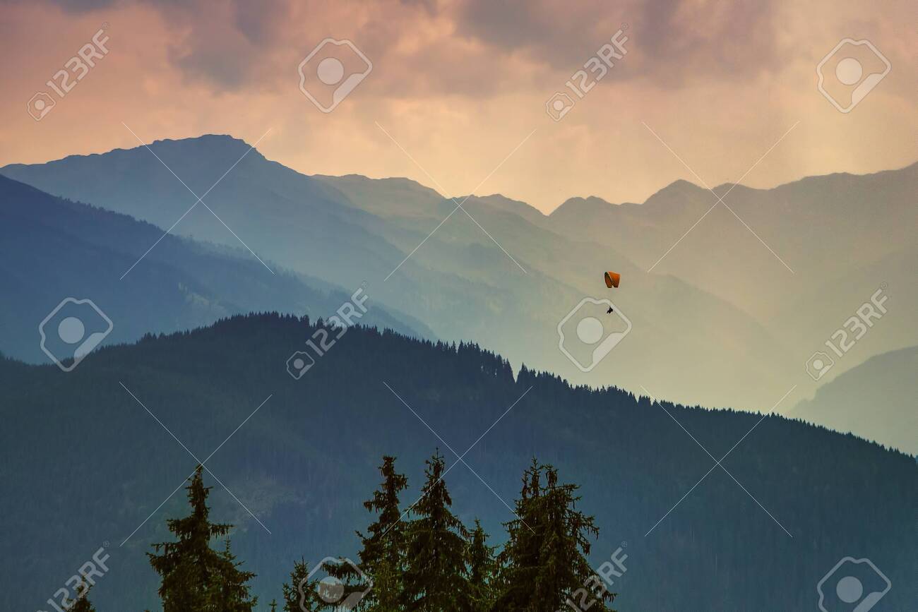 Moody picture of evening mountain ridges, Austrian alps, with a small paraglider on a horizon. - 128379512 Moody picture of evening mountain ridges, Austrian alps, with a small paraglider on a horizon. - 128379512