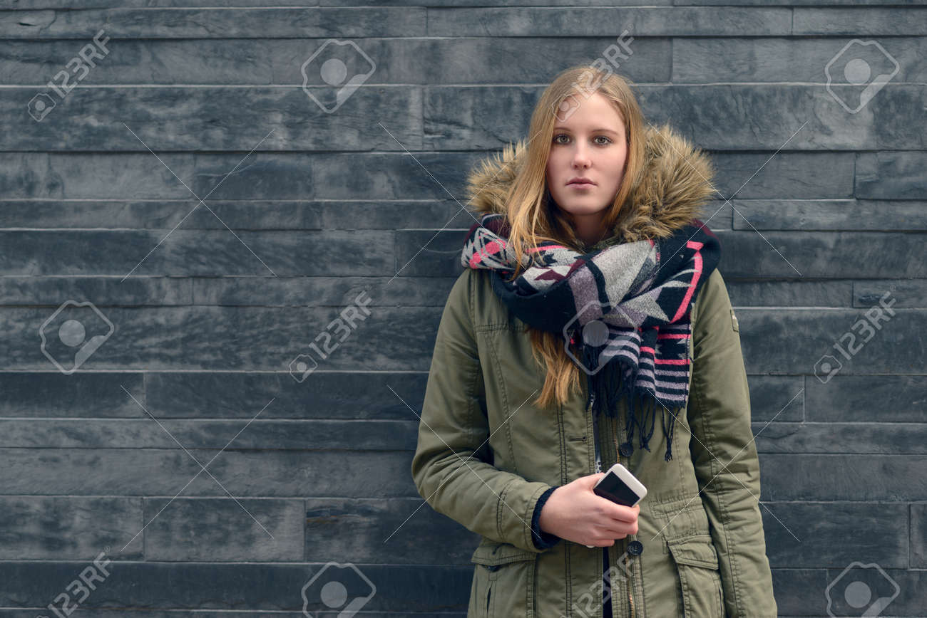 Banque d\u0027images , La mode jeune femme en hiver Outfit posant devant Vieux Mur Gris tout en regardant la caméra.