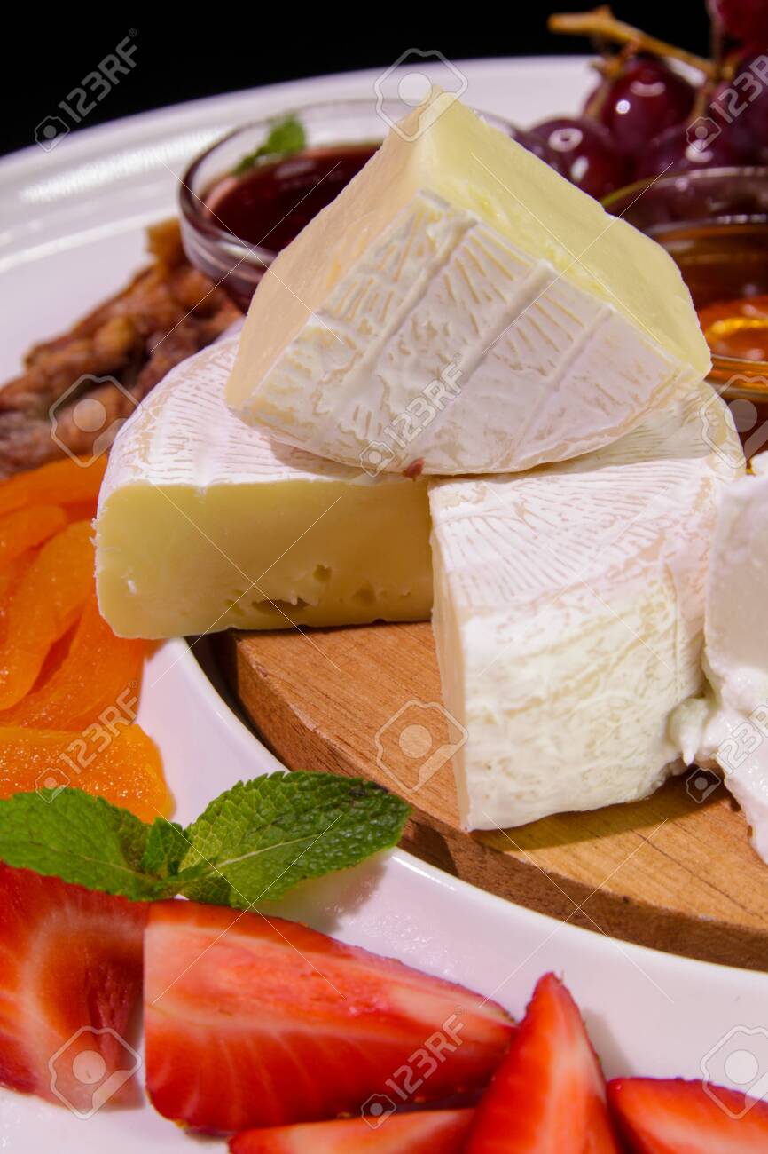 Camembert cheese served with strawberries, dried apricots, mint, grapes, jam on a white plate.Cheese plate. - 141098560 Camembert cheese served with strawberries, dried apricots, mint, grapes, jam on a white plate.Cheese plate. - 141098560