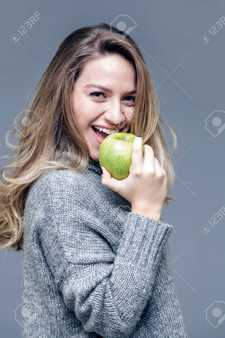 灰色の背景に緑のリンゴを食べて光の茶色の髪の美しい少女 の写真素材 画像素材 Image