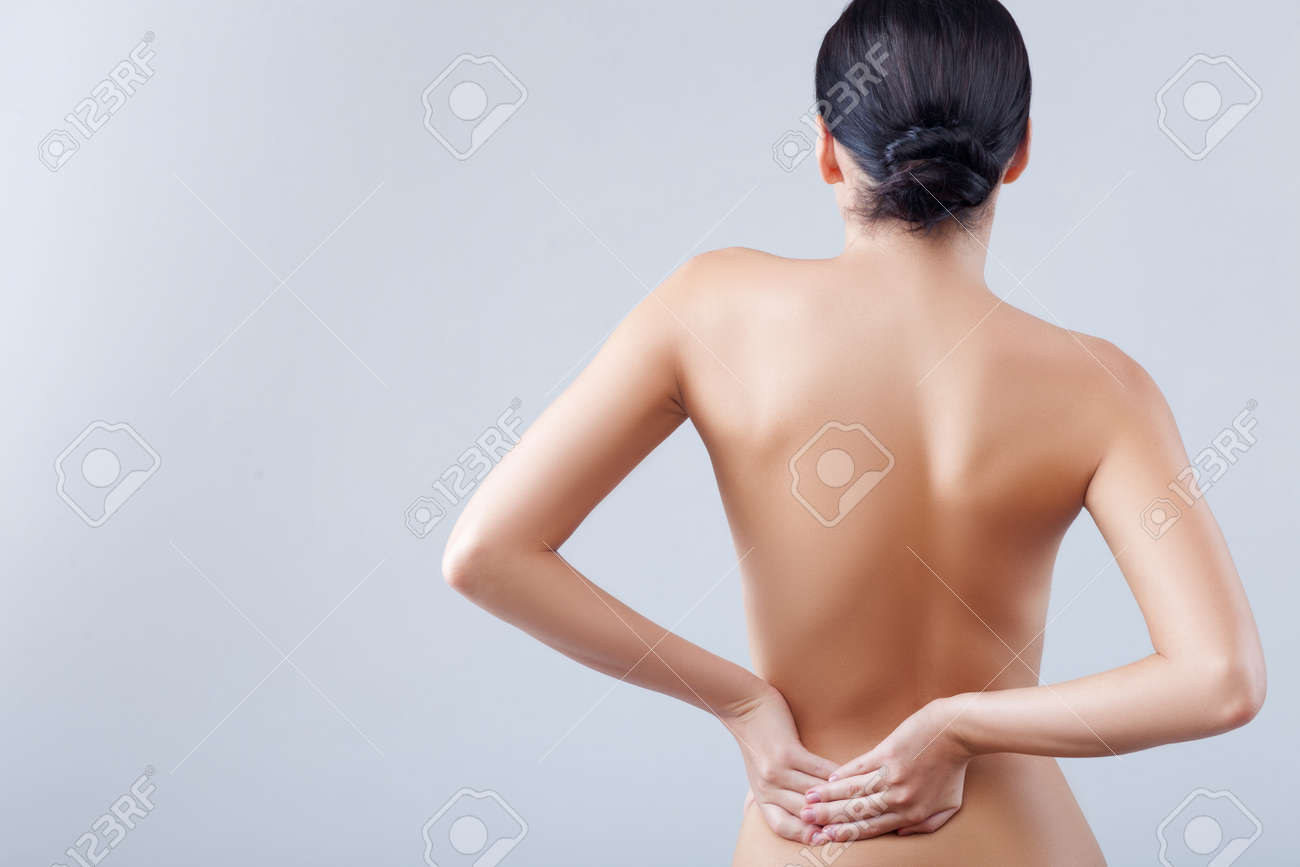 美しい裸の女性が彼女の背中をマッサージします 彼女の腰が痛い 彼女は 立っている 彼女の疲れた体に触れます 分離し 左側のスペースをコピー の写真素材 画像素材 Image