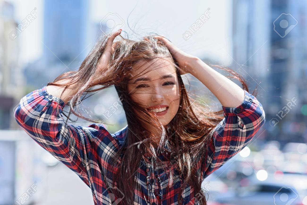 幸せな若い女の子がいちゃつくと笑顔します 彼女は 通りに立っている ポーズします 女性が髪を触ると喜びでカメラを見て の写真素材 画像素材 Image