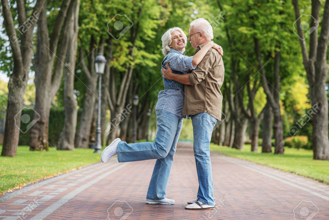 うれしそうな老人と女性の公園でデートしています 路地の上に立って 抱き締めます 愛好家が笑っています の写真素材 画像素材 Image