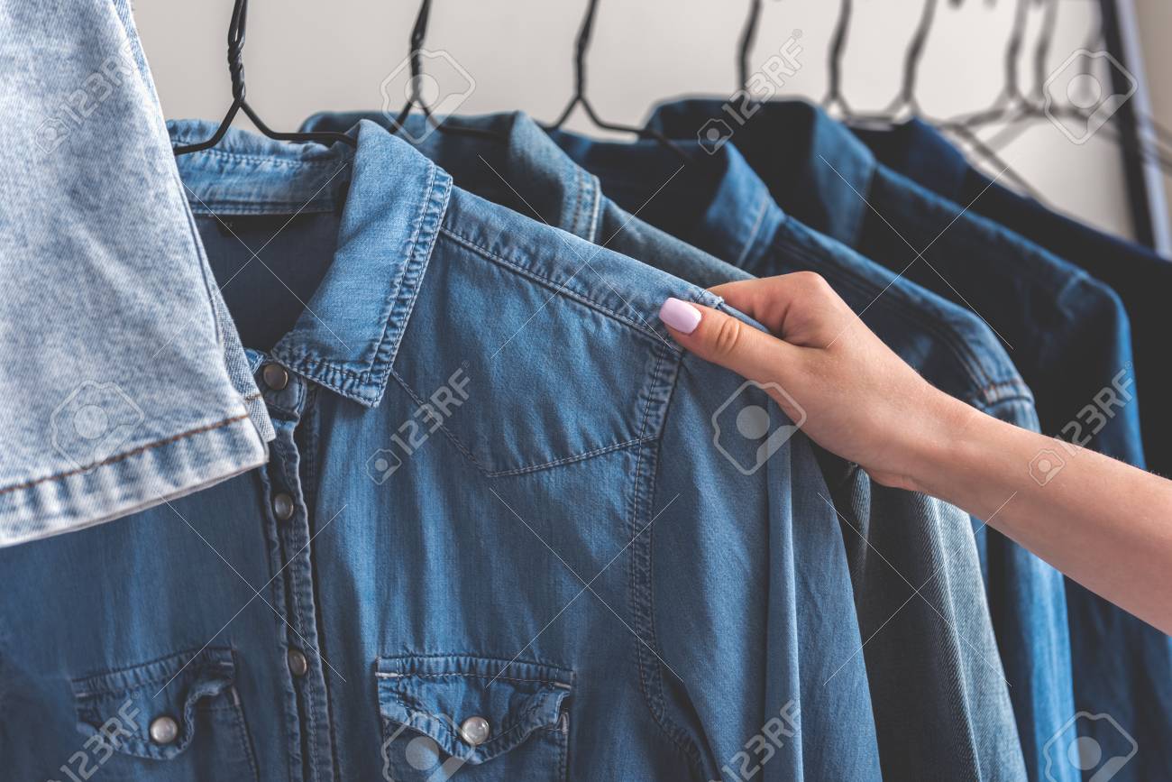 La Chica Va A Llevar Una Camisa De Jean Varias Chaquetas Están En Perchas Ciérrese Para Arriba De La Cosa Femenina De La Toma De La Mano Copie El Espacio A La