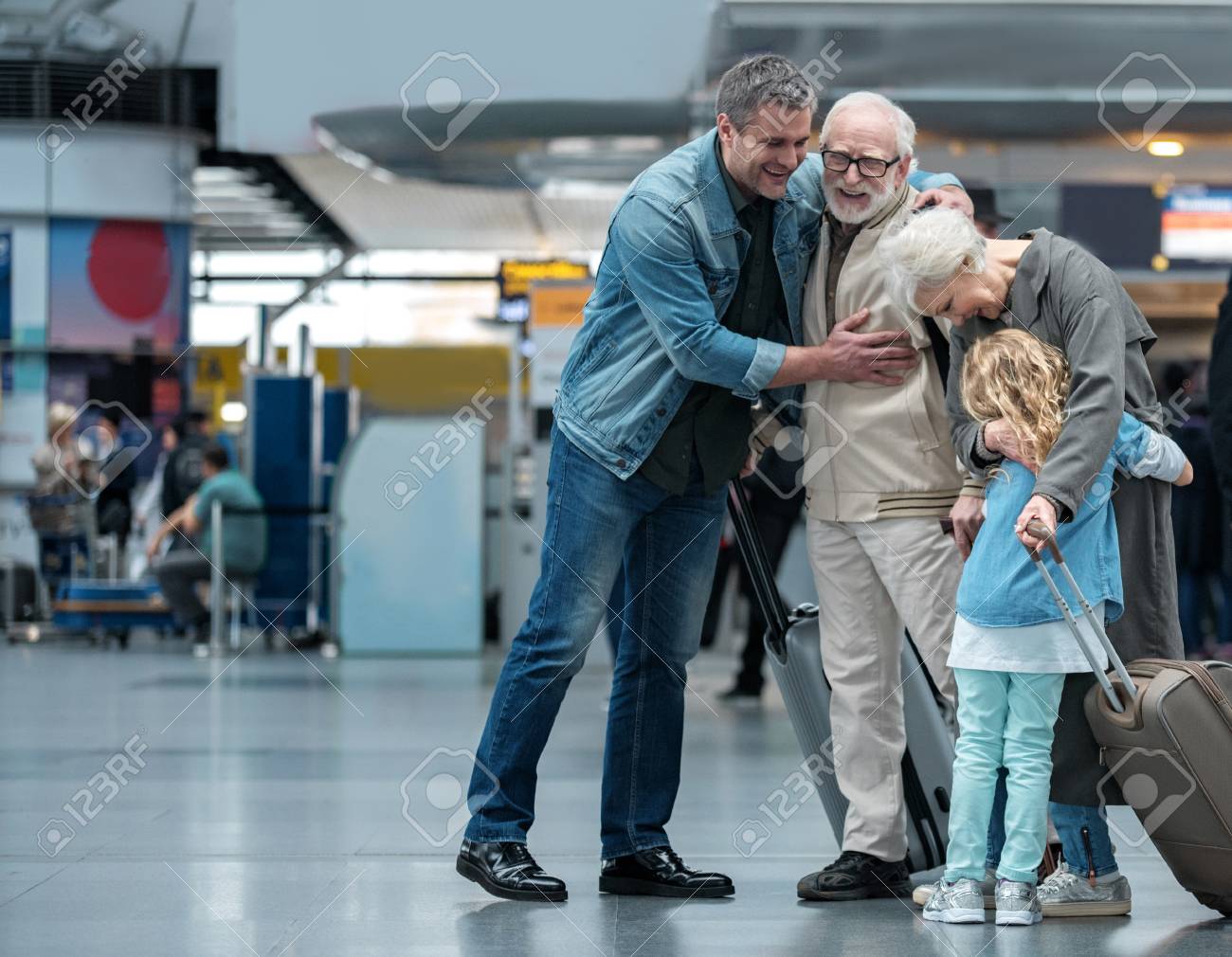 Happies moment. Full length of aged father is hugging his adult sun and expressing gladness. Old joyful woman is embracing her little grandchild while standing in waiting hall at airport. Copy space - 92228583 Happies moment. Full length of aged father is hugging his adult sun and expressing gladness. Old joyful woman is embracing her little grandchild while standing in waiting hall at airport. Copy space - 92228583
