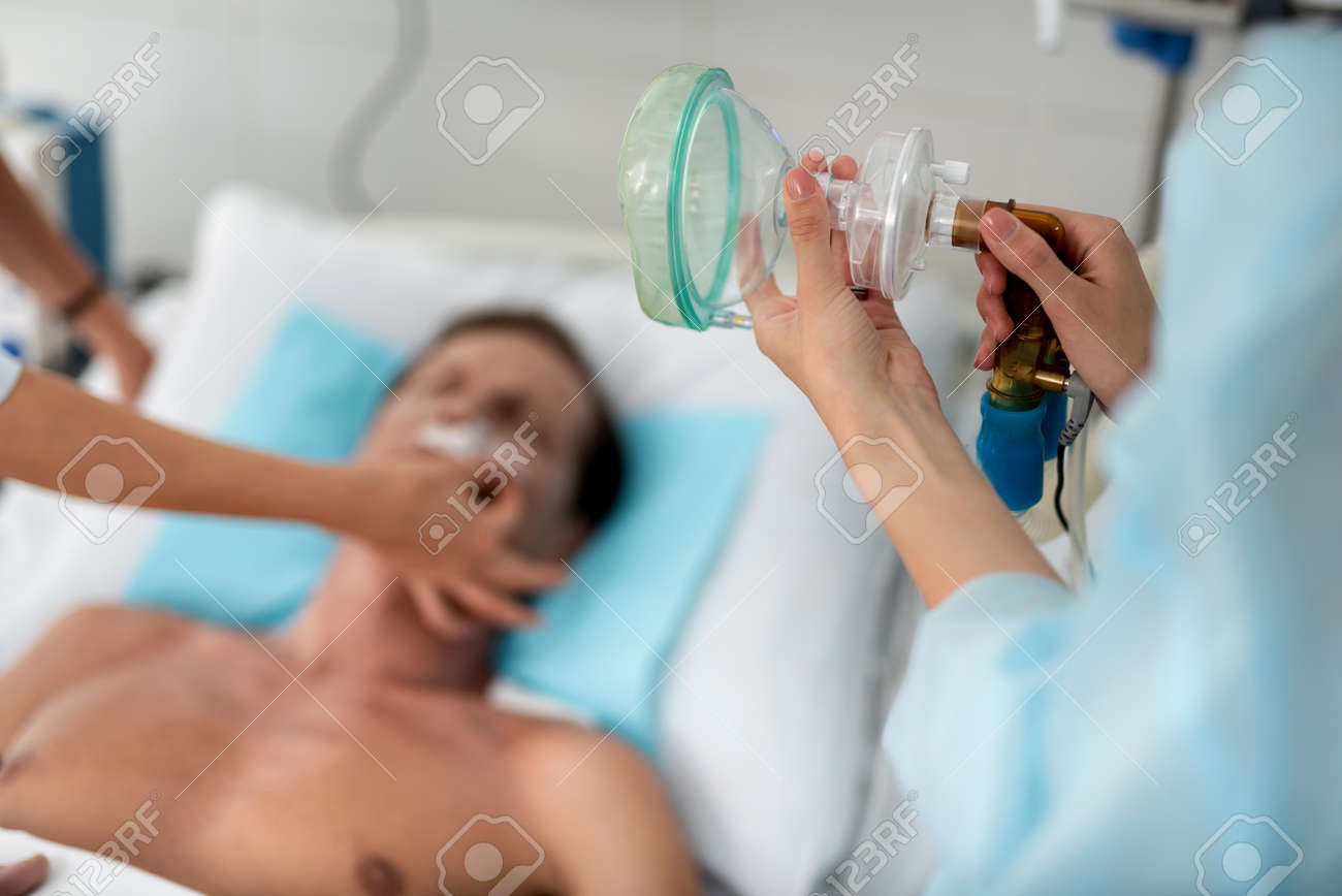 Close up of female hands holding medical respiratory equipment. Man lying on hospital bed and doctor arm on blurred background - 109484094 Close up of female hands holding medical respiratory equipment. Man lying on hospital bed and doctor arm on blurred background - 109484094