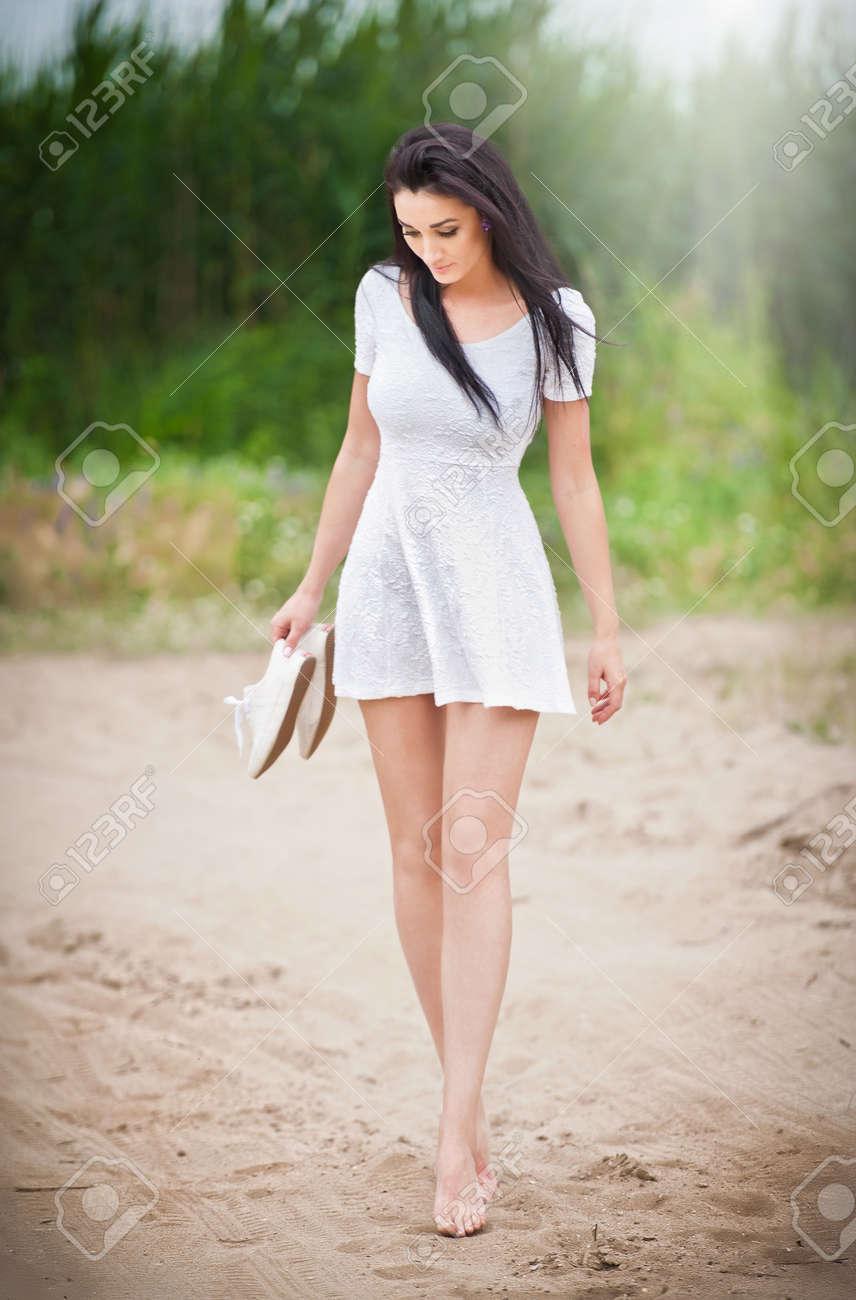 裸足の田舎道を散歩短い白いワンピースの魅力的なブルネットの少女 背景の森と手を靴で歩いて若い美しい女性 屋外の長い脚の女性 の写真素材 画像素材 Image