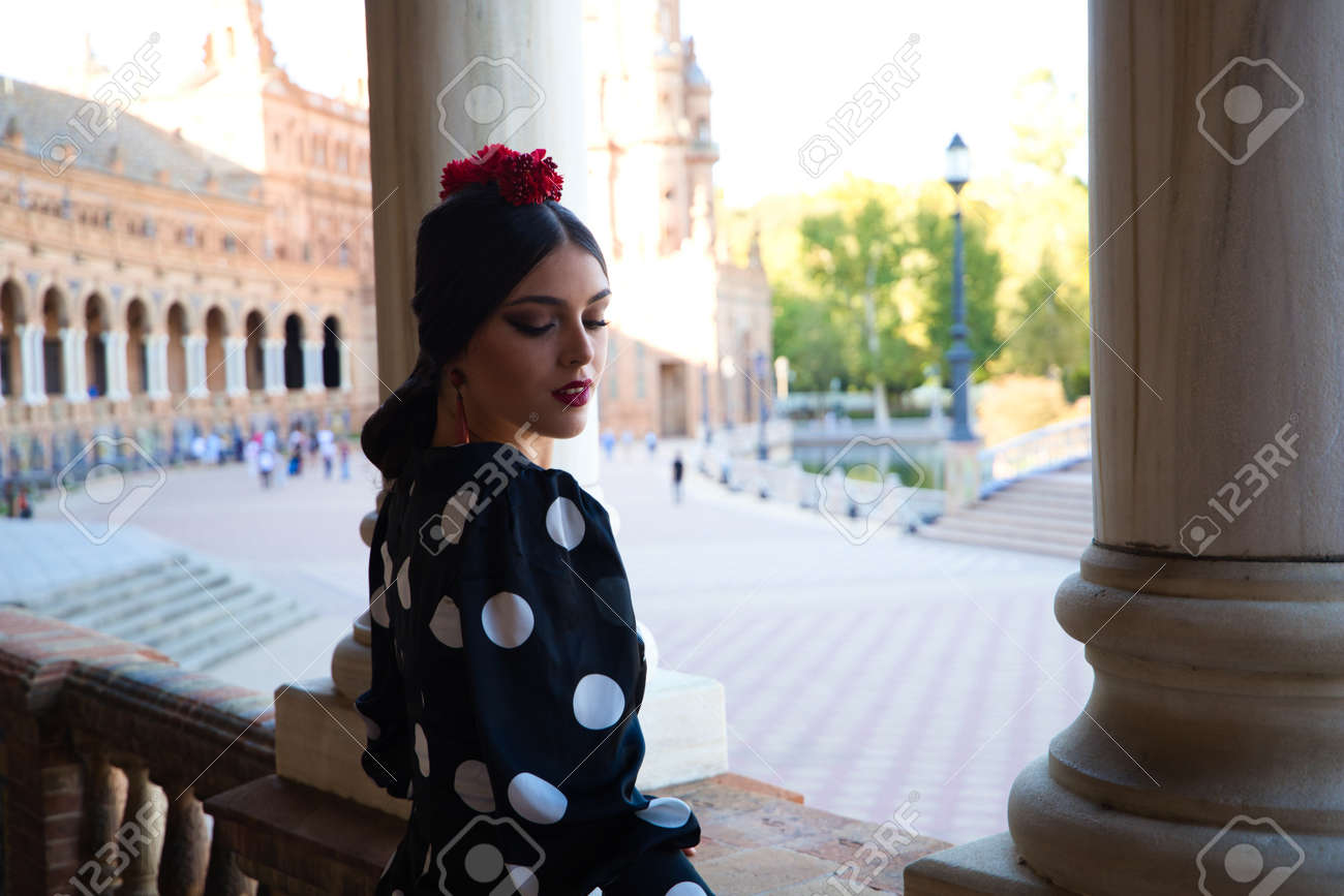 Spanish, Beautiful, Brunette Flamenco Dancer With A Typical Flamenco Dress  In Black With White Polka Dots. She Is In The Plaza Spain In Seville.  Flamenco Concept Cultural Heritage Of Humanity. Stock Photo,