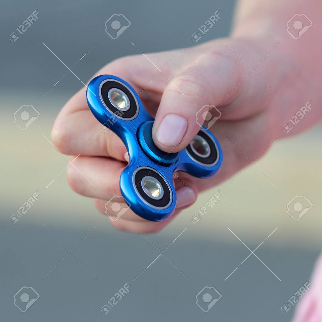 女の子の人気を保持している通り 女性の手に手に青い金属スピナーを演奏そわそわ不安の救済グッズ ストレスとリラクゼーションのそわそわしたアンチ 灰色の背景にスピナー グッズ の写真素材 画像素材 Image