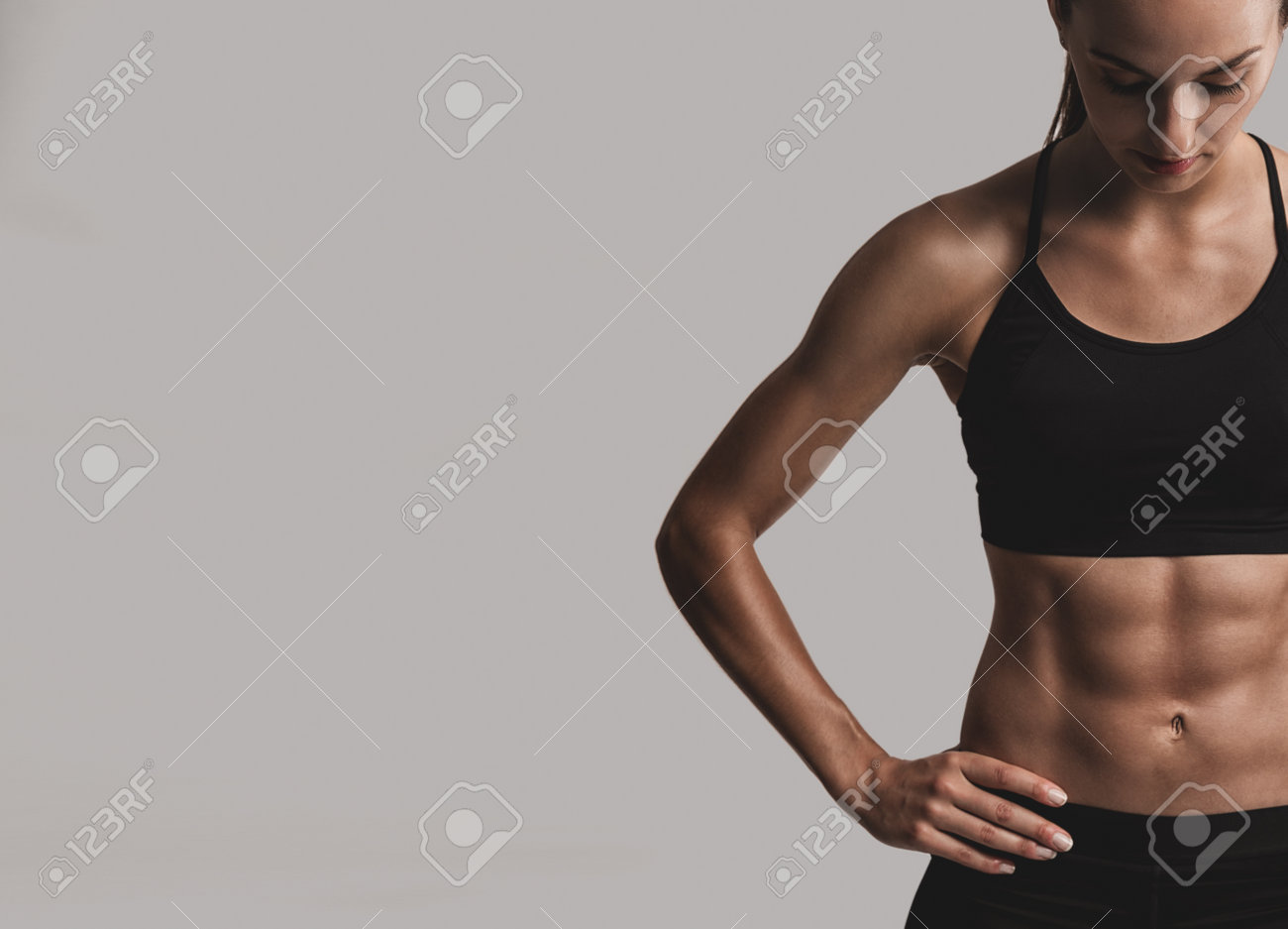 Portrait of sporty young woman with muscular body, posing against a gray background - 75665954 Portrait of sporty young woman with muscular body, posing against a gray background - 75665954