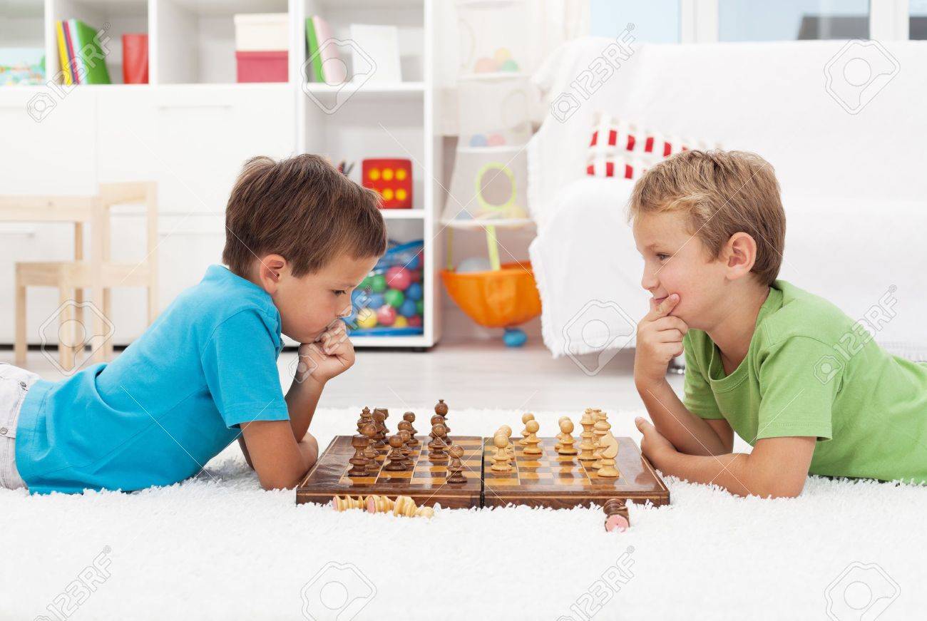 Kids playing chess. Two boys, aged six and eight years, think