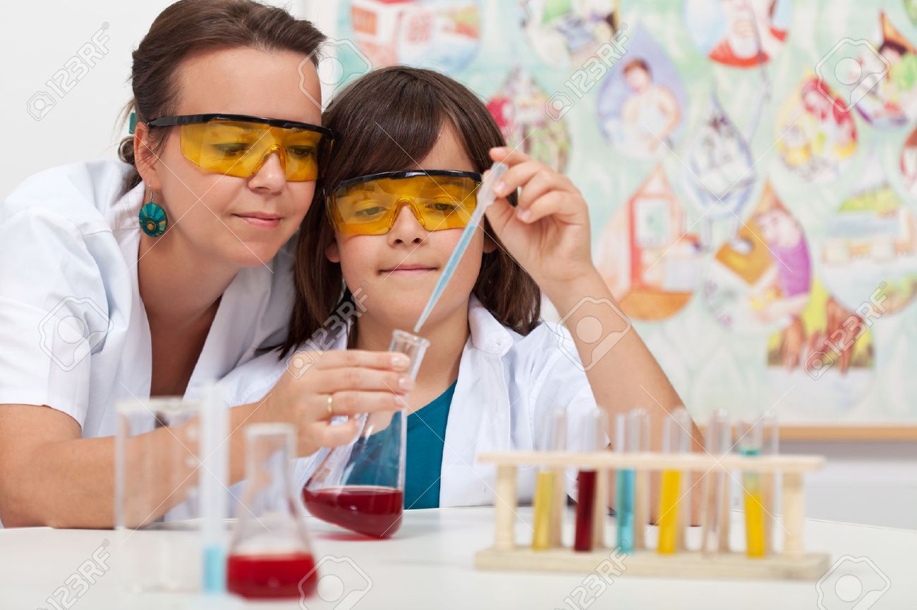 Young boy in elementary science class doing chemical experiment helped by teacher - 47114916 Young boy in elementary science class doing chemical experiment helped by teacher - 47114916