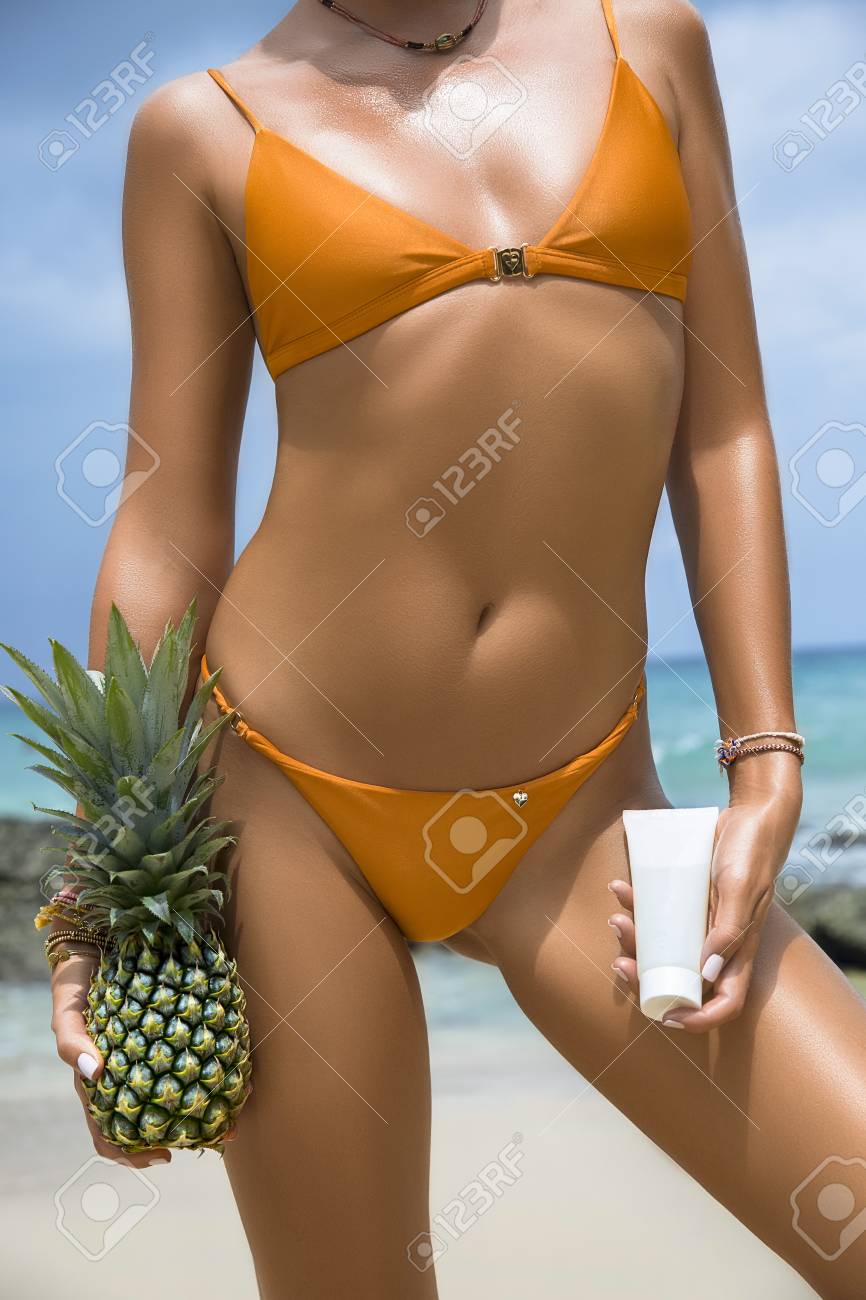 海のビーチで水着姿の美女の裏スリムなクローズ アップの美しい高級 手の中のセクシーな日焼けした体 パイナップル 日焼け止めクリーム 熱帯の島の残りの部分します セクシーなお尻 の写真素材 画像素材 Image