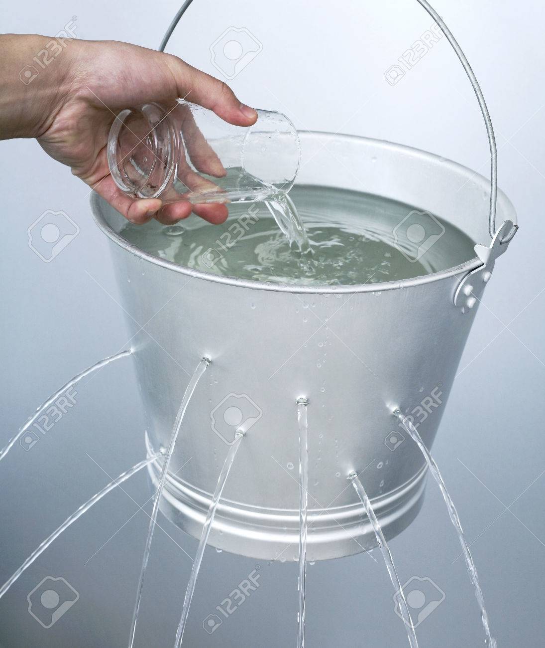 hand pouring water from a glass into a leaking pail stock photo