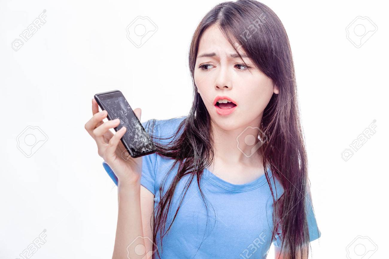 Asian woman looking at broken smartphone in disbelief - 47687908 Asian woman looking at broken smartphone in disbelief - 47687908