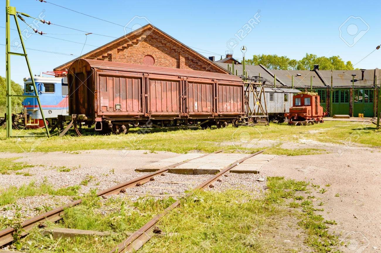 Abandoned Trains And Cars Outside An Old Service Depot With Railroad Tracks  Leading Up To Building. Small Railway Crossing In Foreground. No Person  Visible. Stock Photo, Picture and Royalty Free Image. Image, image size:1300x864