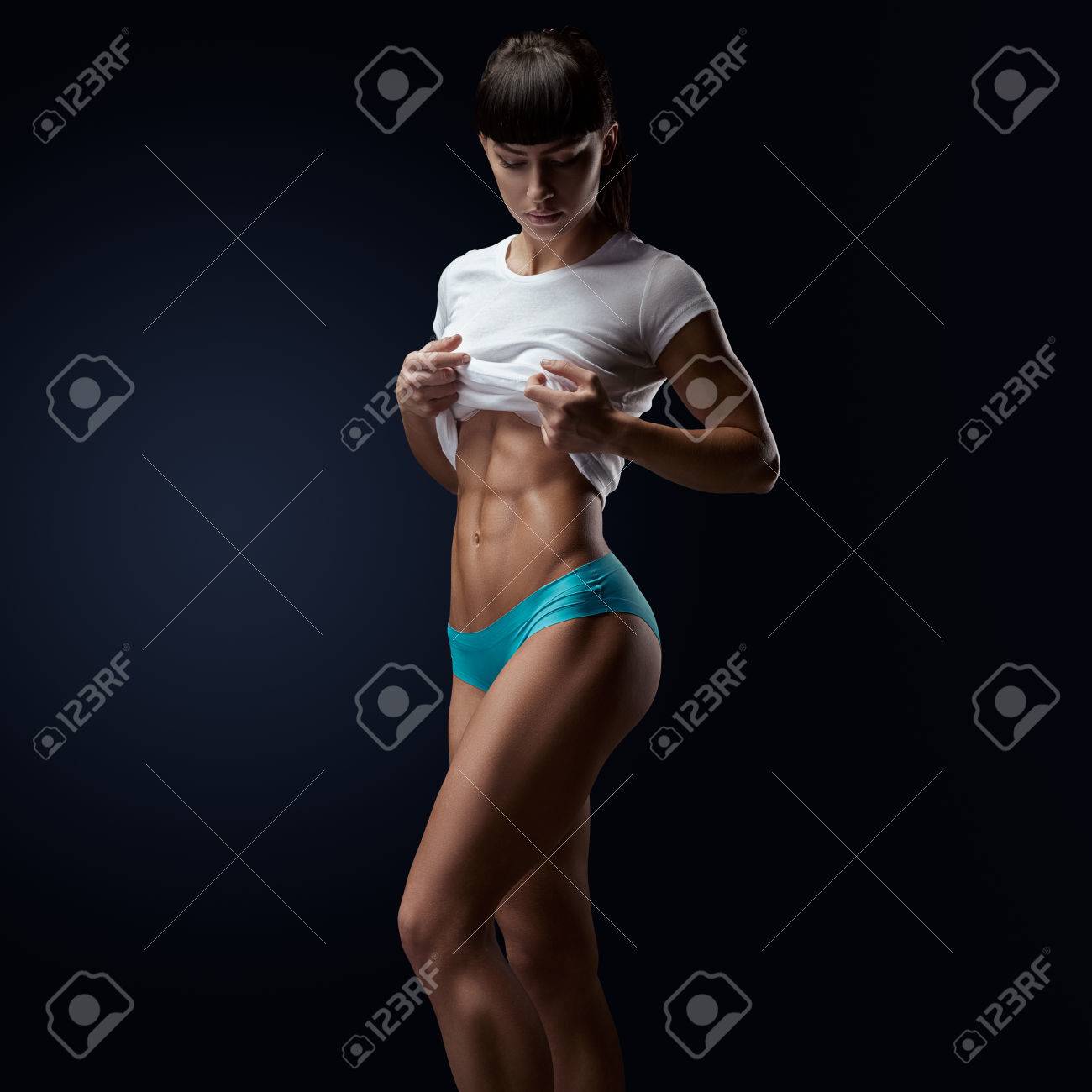 フィットネス運動の若い女性は 彼女をよく見せて形ボディ 6 パック 完璧な腹筋 肩 上腕二頭筋 上腕三頭筋と胸 三角筋 コピー スペースと暗い背景の写真 の写真素材 画像素材 Image