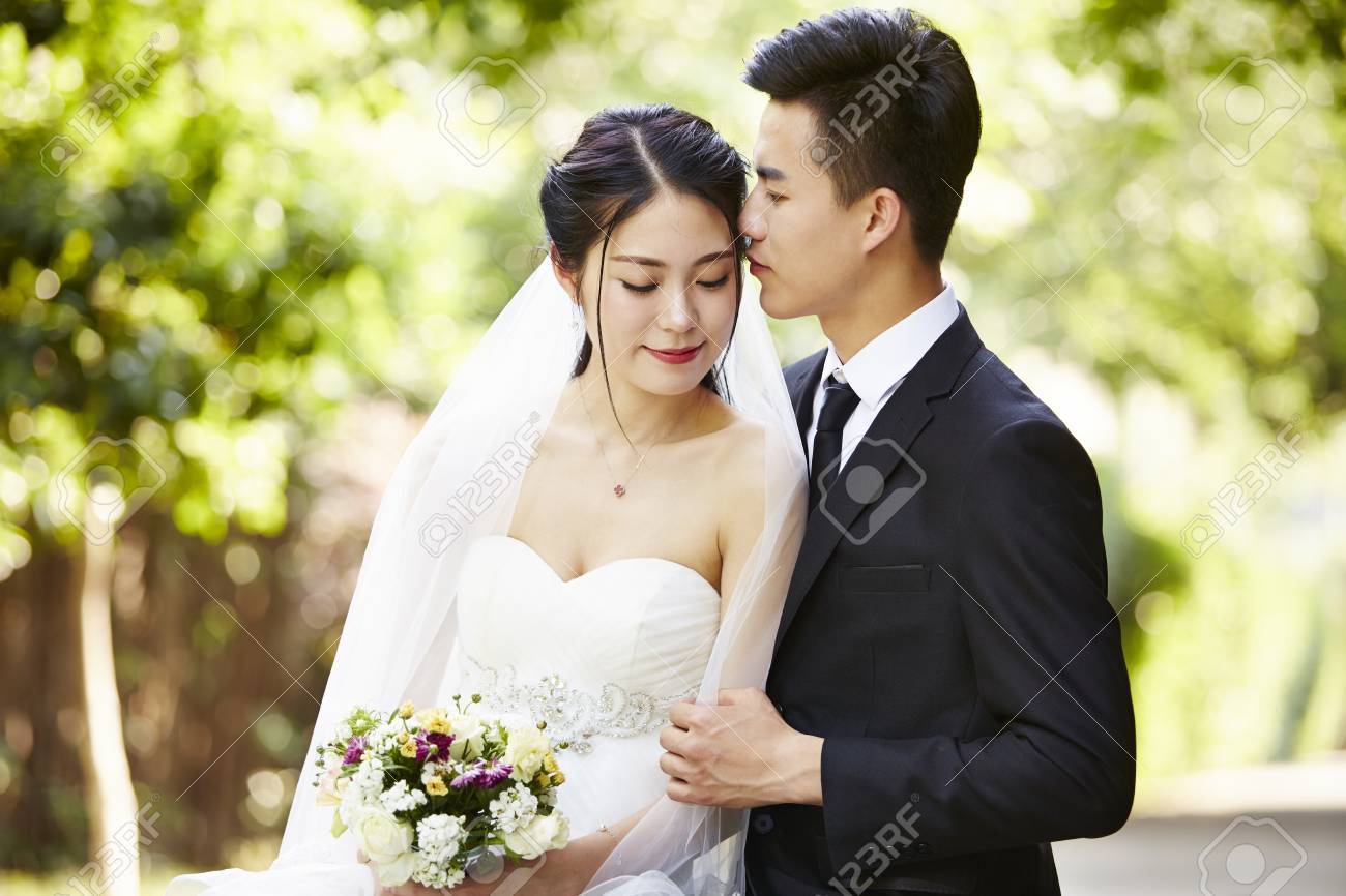 young asian groom kissing bride outdoors during wedding ceremony. - 86610110 young asian groom kissing bride outdoors during wedding ceremony. - 86610110