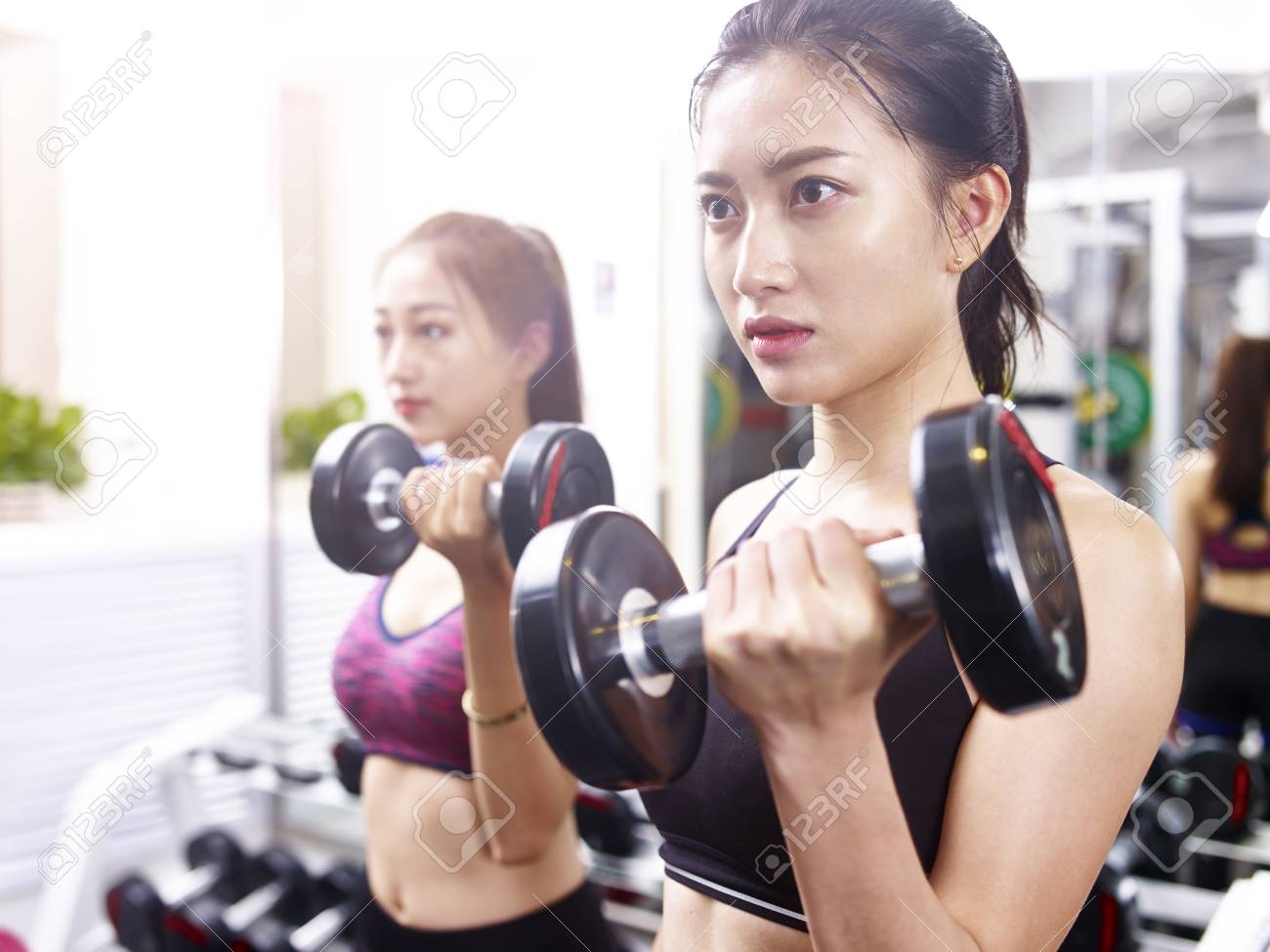 two young asian women working out exercising in gym using dumbbells. - 89328939 two young asian women working out exercising in gym using dumbbells. - 89328939