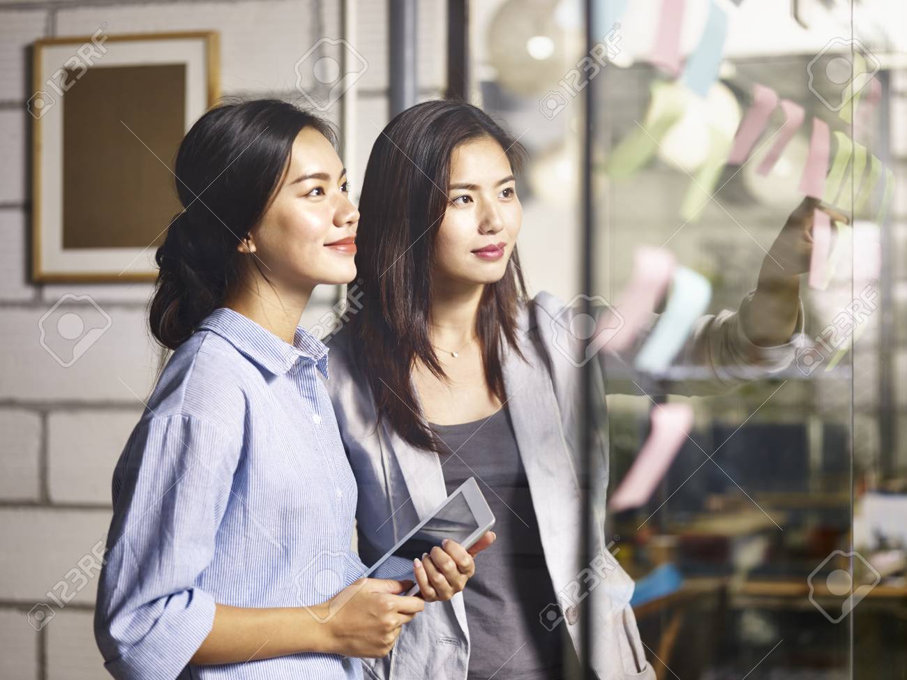 two young asian women entrepreneurs discussing business plan in office using sticky notes. - 90955902 two young asian women entrepreneurs discussing business plan in office using sticky notes. - 90955902