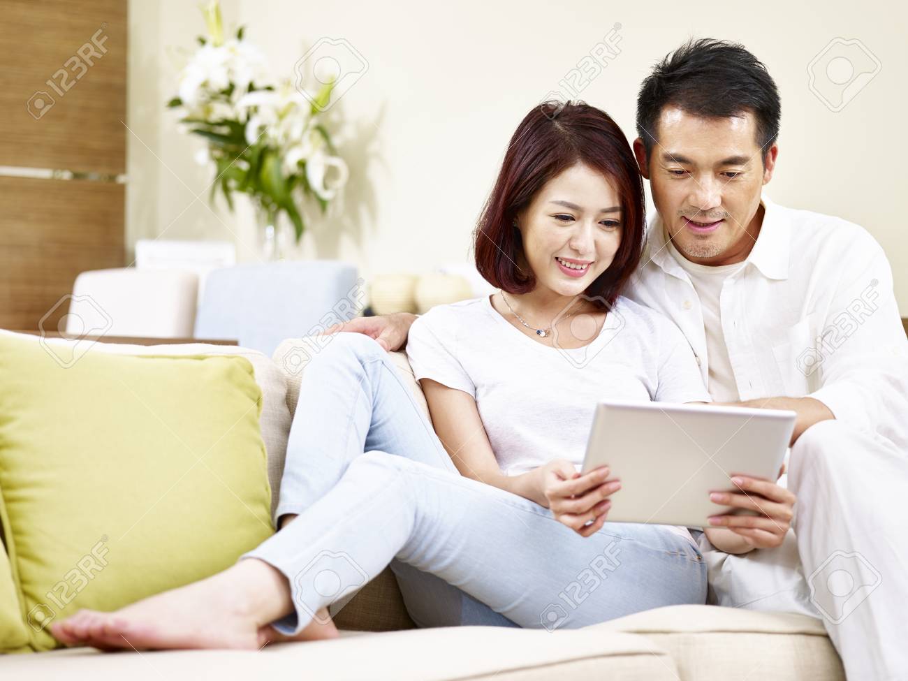 asian couple sitting on family couch in living room using digital tablet together. - 91879462 asian couple sitting on family couch in living room using digital tablet together. - 91879462