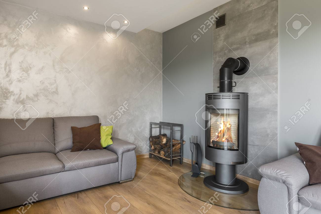 Salon gris avec canapé, cheminée en style industriel, panneaux de sol en bois et finition murale décorative